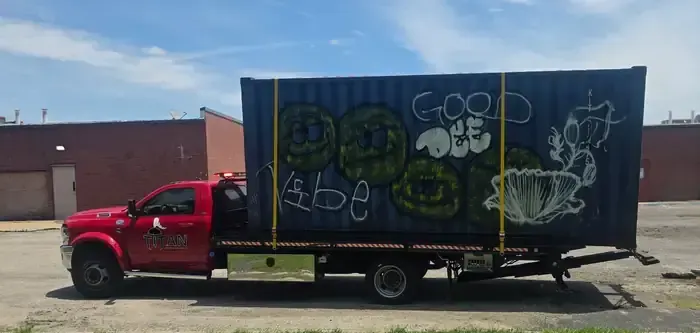 Titan red rollback flatbed hauling a shipping container.